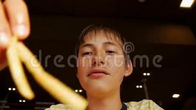 青少年吃快餐。 在快餐店里，青少年男孩咬薯条的特写镜头。